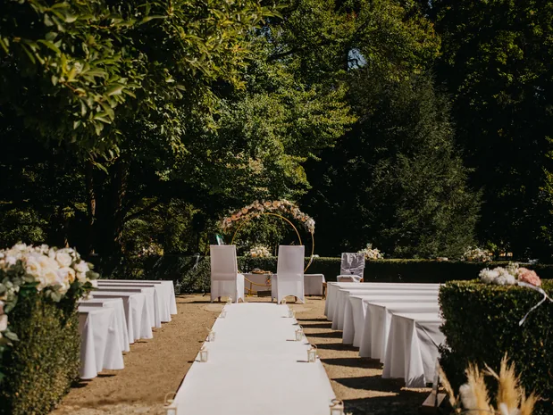 Aufgebaute freie Trauung im Schlosspark Hellbrunn mit Stuhlreihen, Mittelgang und Blumenbogen